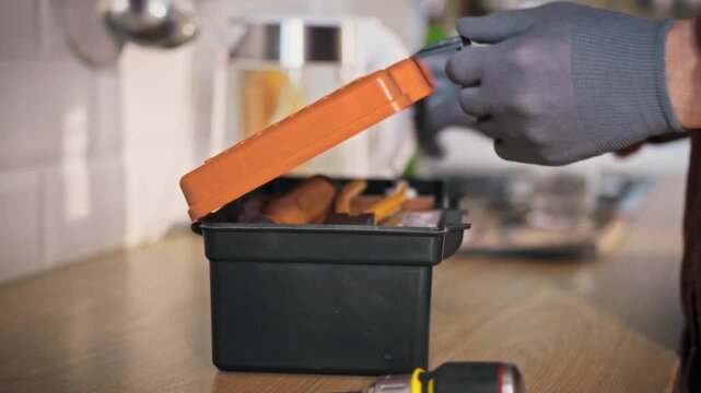 A specialist in work uniform arrives in a home kitchen and sets down a toolbox on the table ready to begin repair work. Concept of calling a professional technician for domestic repairs