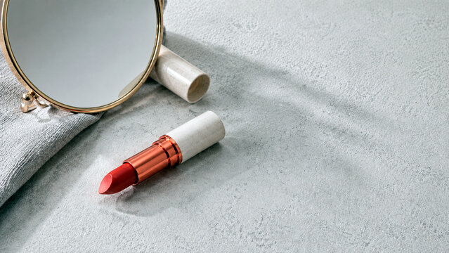 Red lipstick with mirror on table. Cosmetic beauty product for makeup application. Luxury fashion accessory for woman. Morning skincare routine and personal style grooming concept.