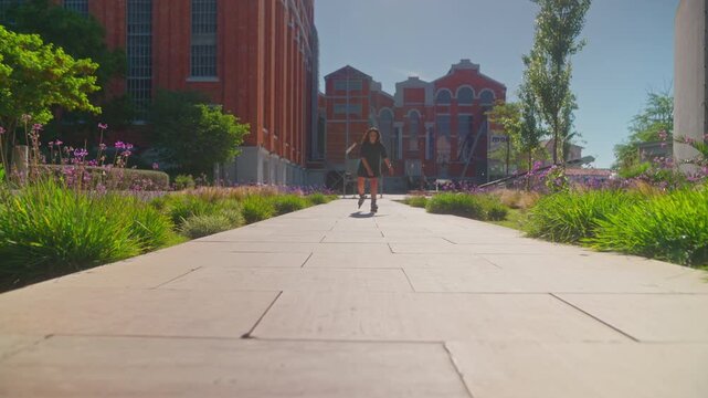 Skater Gliding Through a Vibrant Urban Pathway Surrounded by Lush Greenery and Colorful Flowers in Bright Sunshine