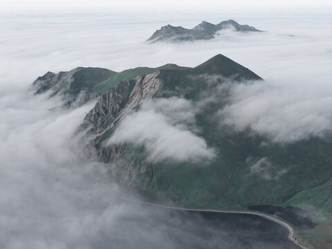 Aerial view of the rugged green mountains of Unalaska rising above a thick layer of low-lying clouds near the coast in Unalaska, Alaska, United States.