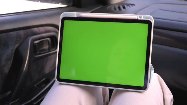 Tablet with green screen held in car. Hands steady, focused on device. Perfect for overlaying apps or navigation visuals. Ideal for travel, tech, or automotive marketing