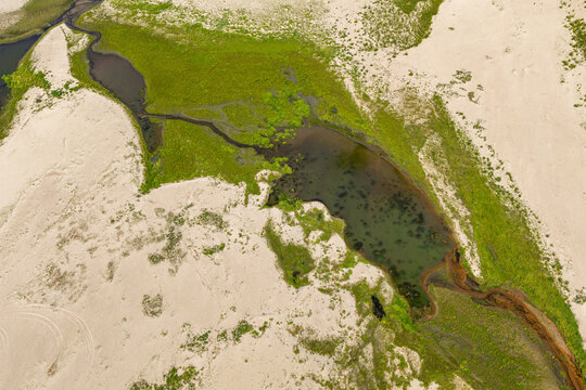 Aerial view of a sandy landscape featuring a small pond with green vegetation and natural textures in Poland.