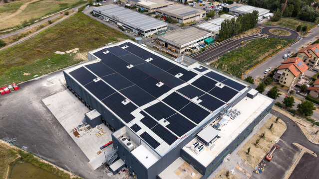 Aerial view of a modern agri-food logistics hub featuring a large rooftop solar panel array, ventilation systems, and loading docks in an industrial area Melegnano, Lombardy, Italy.