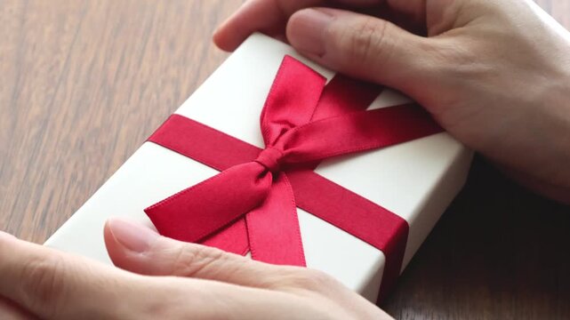 木製テーブルの上でプレゼントの赤いリボンを結ぶ女性の手のアップ