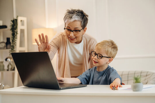 Senior woman and young boy smiling while video chatting on a laptop at home, modern interior with soft lighting and decorative elements visible in the background