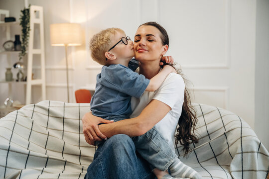 Caucasian woman and young boy embrace on a couch in a cozy living room, with soft lighting and decorative elements visible in the background