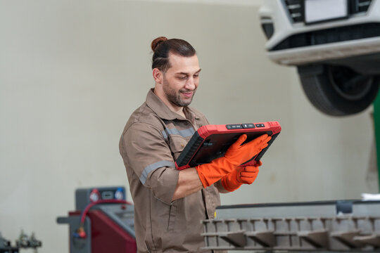Mechanic tablet car repair glove garage inspection, smiling male technician using digital device under lifted vehicle