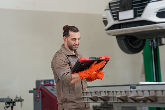 Mechanic, car, tablet, glove, garage technician inspects raised vehicle with digital device during automotive service work