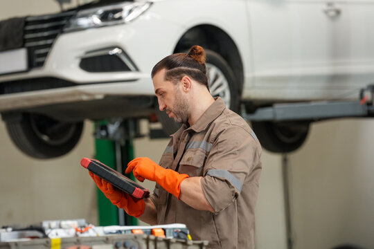 Mechanic car tablet glove garage repair service vehicle checkup in workshop with lifted automobile and focused worker