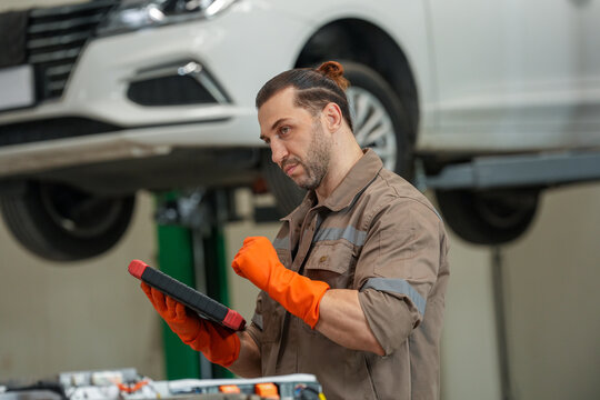 Mechanic car tablet glove garage repair lift vehicle focused technician uses digital device during auto service