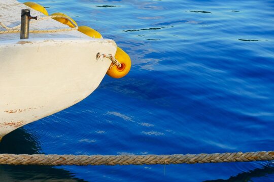 White fishing boat with yellow buoy and rope in harbor on the blue sea surface, sea nautical equipment