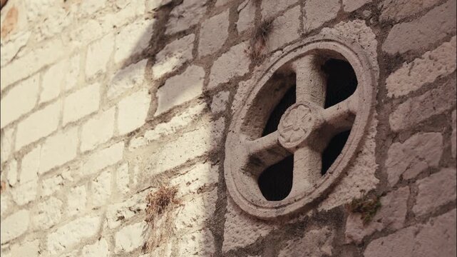 Circular stone rose window with carved cross motif is set into the weathered stone wall of a historic church.