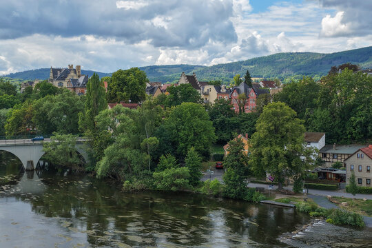 Aerial view of the town of Saalfeld along the Saale river with a bridge, historic buildings, lush green trees, and rolling hills in the background in Saalfeld, Thuringia, Germany.