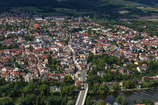 Aerial view of the historic town of Saalfeld with traditional rooftops, church spires, and the Saale river flowing through the green landscape in Saalfeld, Thuringia, Germany.