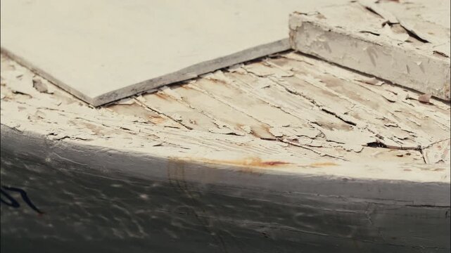 Close up of a weathered wooden boat deck with peeling paint and signs of age above calm water.