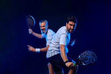 Fototapeta premium Padel tennis doubles. Two athletes players with racket. Man athlete with paddle racket on court with neon colors. Sport concept. Download a high quality photo for the design of a sports app