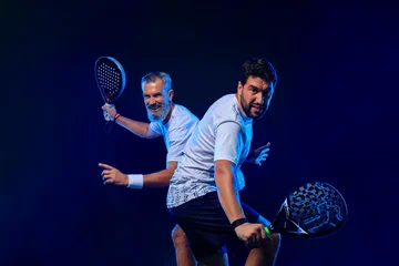Padel tennis doubles. Two athletes players with racket. Man athlete with paddle racket on court with neon colors. Sport concept. Download a high quality photo for the design of a sports app © Mike Orlov