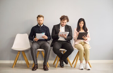 Obraz premium Candidates interview hiring recruitment applicants waiting with paperwork. Three business applicants fill resume and notes before assessment. Clear hiring recruitment and assessment concept.