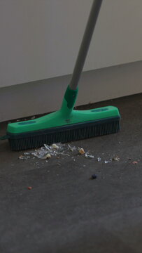 Person carefully gathers shattered glass from her kitchen floor after a household accident, managing danger, injury prevention and practical home maintenance