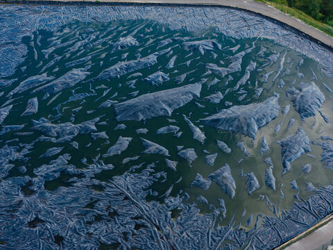 Aerial view of the wastewater sludge storage area with dark textured basins and reservoirs in Riga, Latvia.