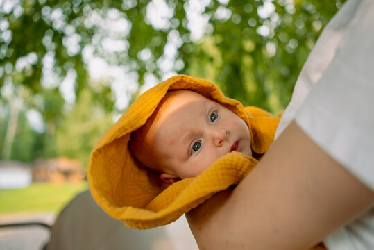 Mother holding newborn baby outdoors, wrapped in a comfortable yellow muslin blanket, symbolizing new life, love, and the tender bond of motherhood and care