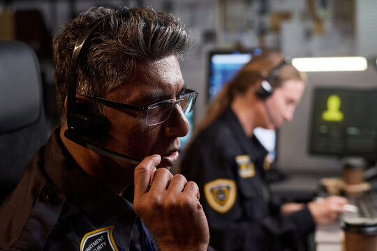 Close up of middle aged man security operator wearing headset, monitoring incident response beside female colleague at control desk. Ideal for emergency dispatch, public safety, support service