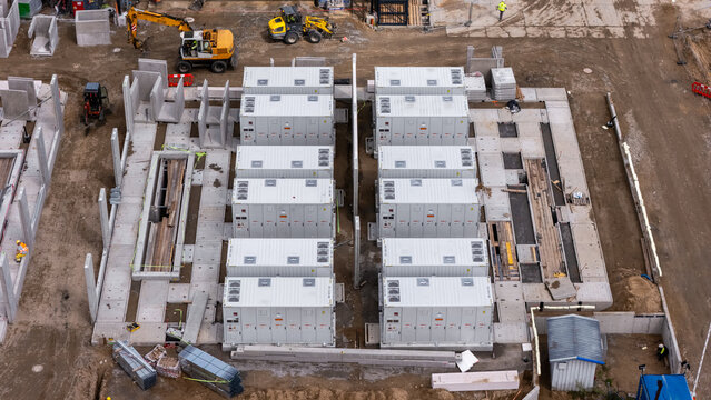 Aerial view of a construction site featuring rows of industrial containers installed on concrete foundations with heavy machinery and workers in Poland.