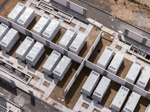 Aerial view of a battery energy storage system with rows of white industrial containers, concrete partitions, and gravel ground in Poland.