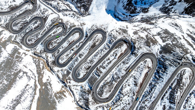Aerial view of the winding switchbacks of Los Caracoles Pass in the Andes mountains with snow-covered slopes and vehicles navigating the road in Portillo, Valparaiso, Chile.