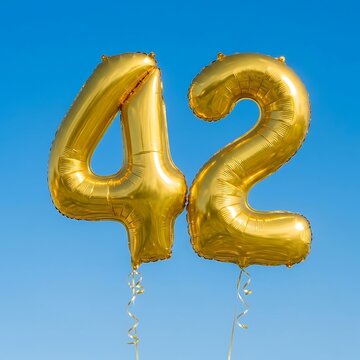 Gold number 42 balloons against blue sky. Shiny metallic foil birthday party decoration.