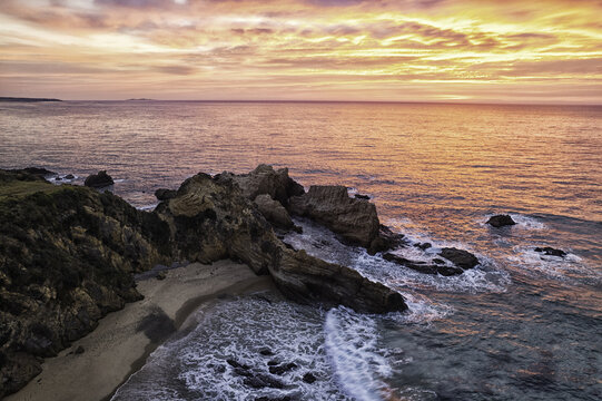 Aerial view of the rugged coastline and rocky formations at sunset with waves crashing against the shore in Bermagui, New South Wales, Australia.
