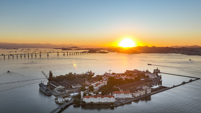Aerial view of Ilha das Cobras in Guanabara Bay at sunset, featuring the Rio de Janeiro Naval Base, industrial buildings, and Rio-Niteroi Bridge in Rio de Janeiro, Rio de Janeiro, Brazil.