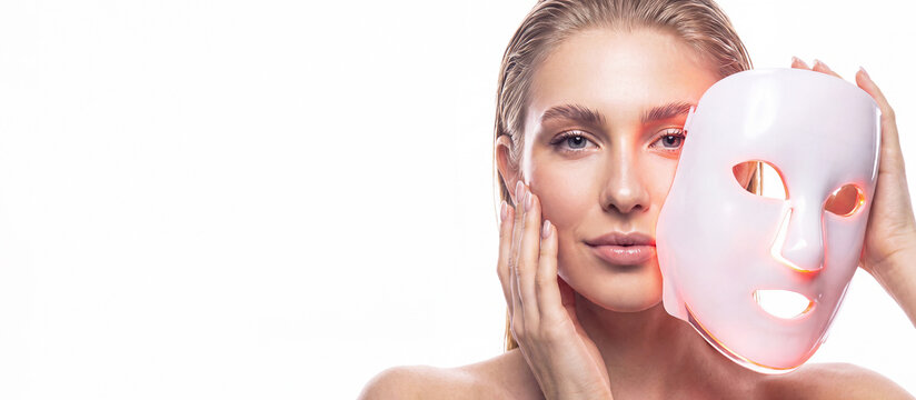 Banner with woman wearing an LED facial mask against a white background with space for text. Professional skin care, rejuvenation, innovative cosmetic technologies, skin healing, and beauty device