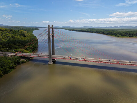 Aerial view of Puente La Amistad spanning the Tempisque River, surrounded by lush tropical forest under a bright blue sky in Bagaces, Guanacaste Province, Costa Rica.