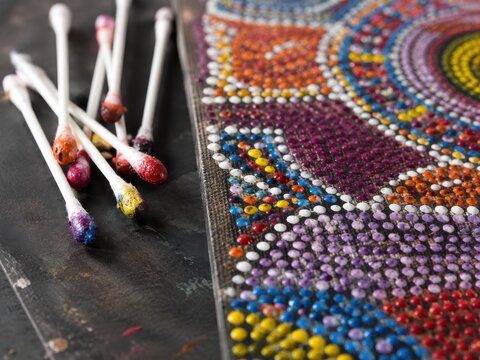Close-up of a Colorful Dot Mandala Painting in Progress with Paint-Stained Cotton Swabs on a Dark Workspace