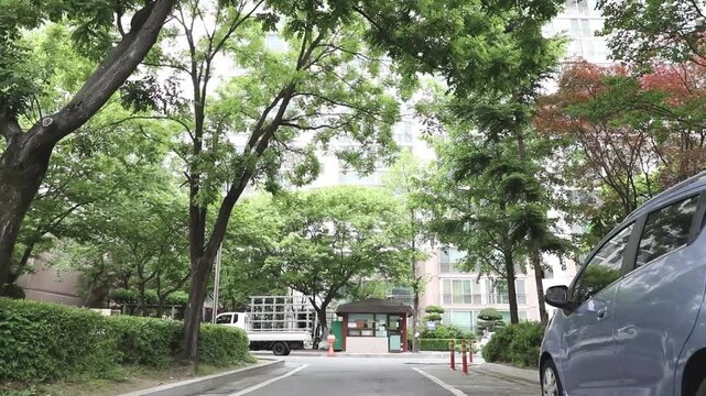 나무 잎사귀 사이로 보이는 아파트 단지와 건물 외관을 올려다보며 촬영한 야외 풍경입니다.