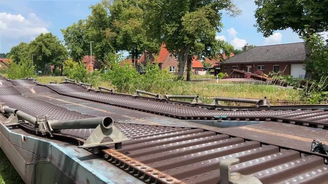 Perspective view along the steel deck of a flat freight rail wagon in Germany. Industrial railway transport, cargo logistics and modern rail infrastructure under bright summer daylight.
