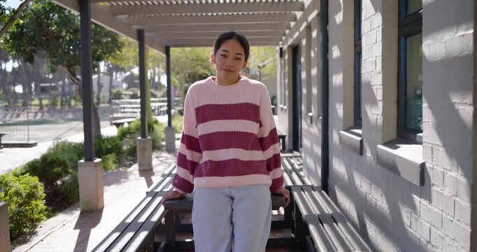 Teenage woman in striped sweater on pergola bench shifting, smiling as camera moving closer posing