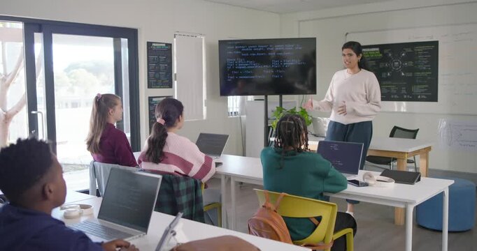 Female teacher pointing at code on monitor explaining code to teens using laptops, copy space