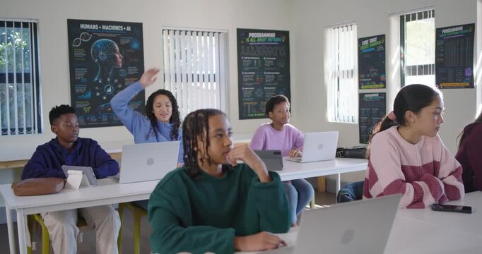 Diverse students, youth female in green sweatshirt responding as teacher entering, guiding laptops