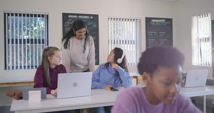 Indian teacher entering and leaning, guiding teenage students in classroom with laptops