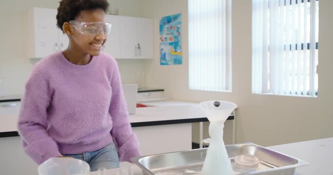 African youth in goggles purple sweater, pouring into funnel over flask during demo, causing foam