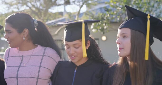 Diverse teens  and  mentor posing linking arms at campus camera pulling back showing gowns caps scro