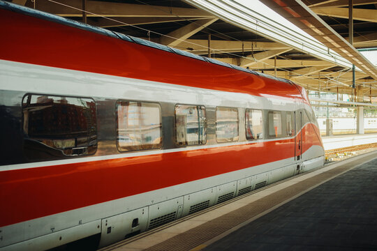 Modern red and white high speed train standing at a covered railway station platform.