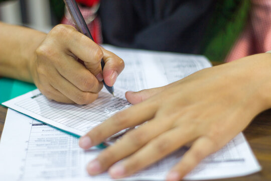 Close up hand filling out a form or exam with pen, paper grid document on desk. Student or employee writing, survey or test paperwork concept.