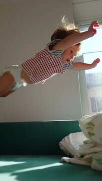 Toddler diving onto couch covered with blankets, celebrating playful energy, fearless exploration and joyful childhood adventure