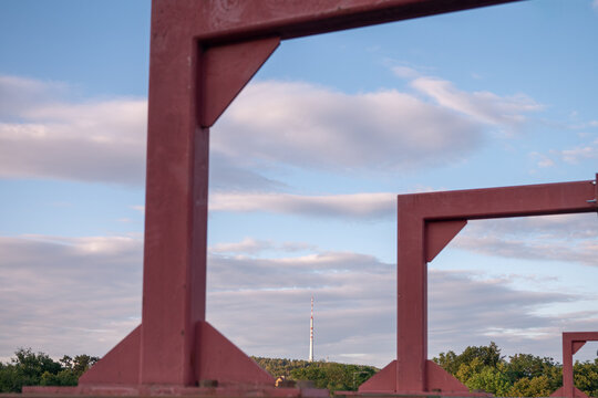Cukr&aacute;k broadcasting tower framed by the steel structure of a temporary pedestrian bridge near J&iacute;lovi&scaron;tě, Czech Republic. Modern engineering, telecommunications and geometric composition at sunset.