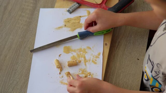 Child Hands Filing Small Piece of Wood with Hand Tool at Desk