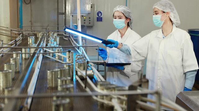 Team female researchers in white quality control suits holds RGB LED lights meticulously inspecting mackerel production line canning sauce filling conveyor belt industrial seafood processing plant.