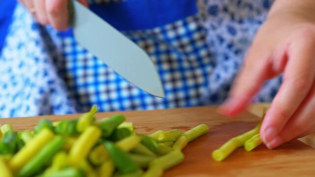 Hands chopping fresh green and yellow string beans with a kitchen knife on a wooden board